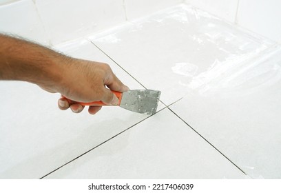 Man uses Trowel to remove old grout. Replace the old grout between the tiles. Mining tiles for rerouting.                       