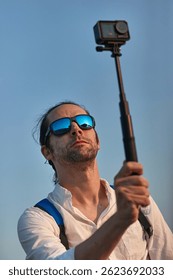 Man using action camera on a selfie stick, shooting travel video vlog
