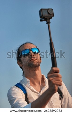 Man using action camera on a selfie stick, shooting travel video vlog