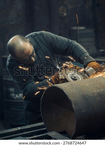 Man using angle grinder to cut steel pipe with sparks in workshop, close up of industrial metalworking process with safety gear and power equipment.