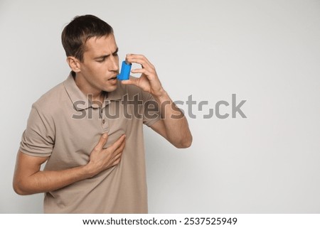 Man using asthma inhaler on light background, space for text