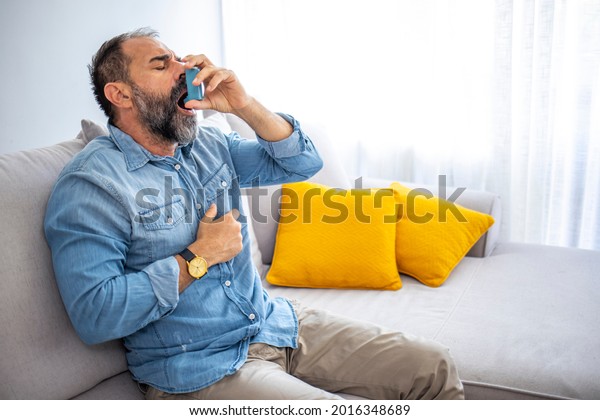 Man using asthma inhaler. Man using asthma\
inhaler for relief an attack at home for preventing attack. Man\
using medical inhaler to prevent and treat wheezing and shortness\
of breath caused by allergy