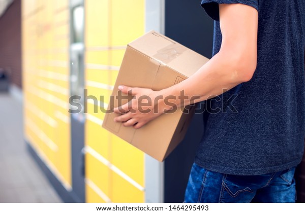Man using automated self\
service post terminal machine or locker to deposit the parcel for\
storage