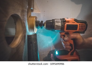 A Man Using A Battery Powered Drill With A Circular Saw Bit To Drill A Hole In A Wooden Plank. Vacuum Cleaner Is Visible To Suck The Excess Dust Away.