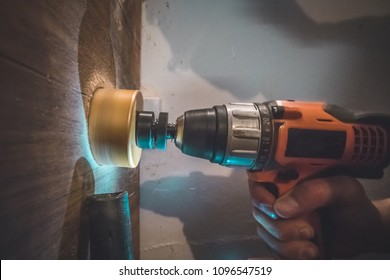 A Man Using A Battery Powered Drill With A Circular Saw Bit To Drill A Hole In A Wooden Plank. Vacuum Cleaner Is Visible To Suck The Excess Dust Away.