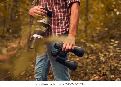 Man using binoculars and camera for birdwatching and other observing animals in nature.