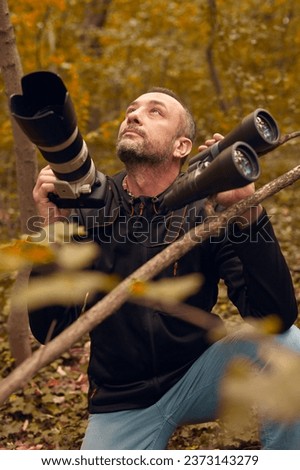 Man using binoculars and camera for birdwatching and other observing animals in nature.