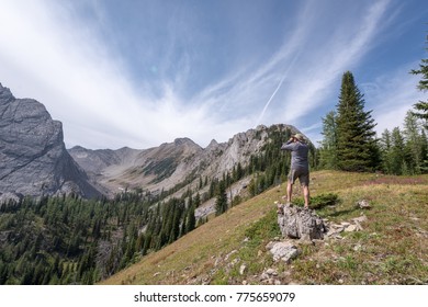 A man using binoculars looking at the beautiful mountain landscape along Pedley Pass hike near the town of Invermere in the Columbia Valley, British Columbia