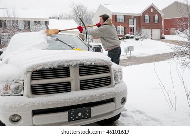 A Man Using A Broom To Sweep Snow Off The Windshield Of His Truck After A Winter Storm.