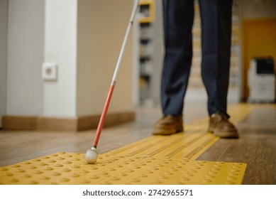 Man using cane for navigation inside library, following tactile paving with feet visible, demonstrating independent mobility for blind individuals