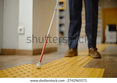 Man using cane for navigation inside library, following tactile paving with feet visible, demonstrating independent mobility for blind individuals