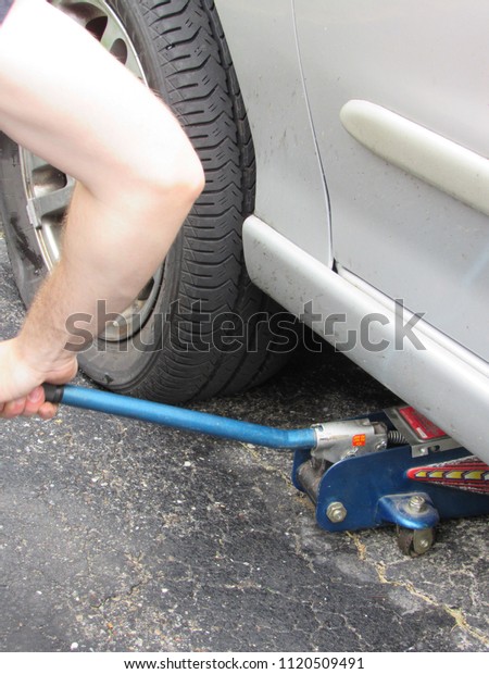 A\
man using a car jack to lift a car to fix a flat\
tire