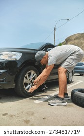 Man using a car jack to replace a flat tire on a black vehicle
