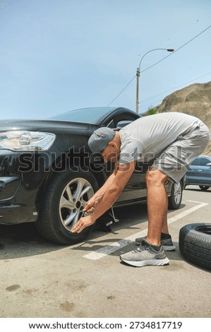 Man using a car jack to replace a flat tire on a black vehicle