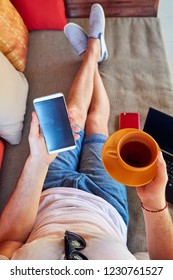 Man using cellphone and laptop while drinking coffee / tea on the porch.