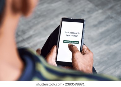Man using cellphone with the message your account is deactivated. Reactivate a cancelled account concept. Digital display, selective focus.