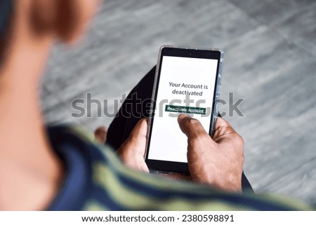 Man using cellphone with the message your account is deactivated. Reactivate a cancelled account concept. Digital display, selective focus.