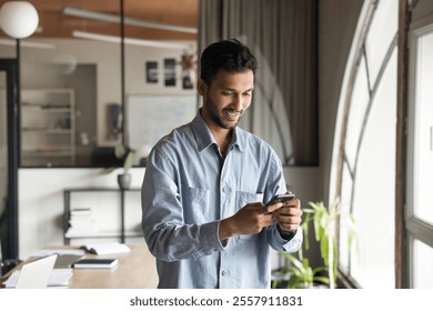 Man using cellphone at workplace, checking messages, responding to emails, communicating with colleagues or clients, smile, engaged in positive interaction related to work. Professional communication