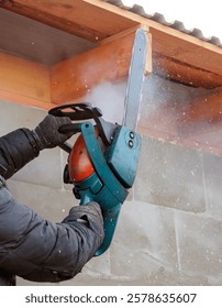 A man is using a chainsaw to cut a piece of wood. The chainsaw is making a lot of noise and is covered in sawdust. The man is wearing gloves and a black jacket