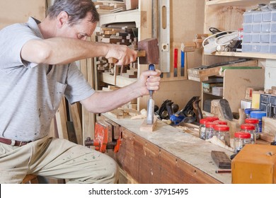 Man using chisel at workbench surrounded by tools and equipment