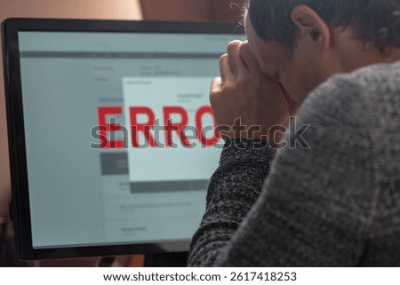 Man using computer with application error message on screen. Man experiencing frustration as he looks at an error message on his computer screen, showcasing his emotional reaction