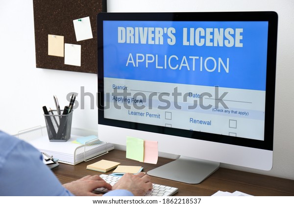 Man using computer to fill driver\'s\
license application form at table in office,\
closeup