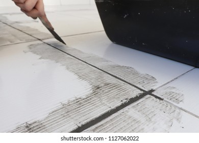 Man Using A Construction Spatula To Put The Grout On The White Ceramic Floor.