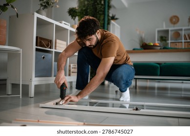 Man using a cordless screwdriver, assembling flat-pack furniture at home. Focus on diy, home improvement, and manual work