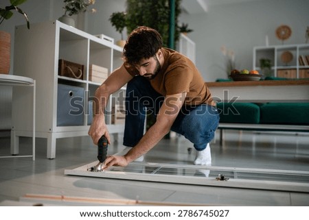Man using a cordless screwdriver, assembling flat-pack furniture at home. Focus on diy, home improvement, and manual work