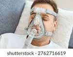 Man using CPAP mask for obstructive sleep apnea treatment on bed at home, top view. Continuous positive airway pressure therapy to stabilize air flow for lying patient for respiratory healthcare