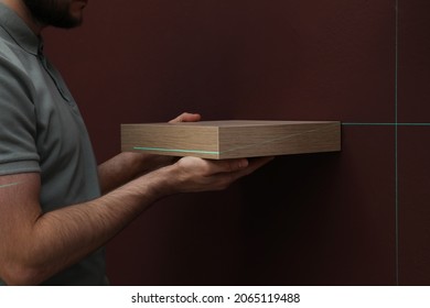 Man Using Cross Line Laser Level For Hanging Shelf On Brown Wall, Closeup