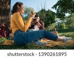 Man using digital camera while woman eating apple on a picnic