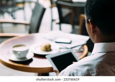 Man using digital tablet while sitting in the cafe, view over his shoulder