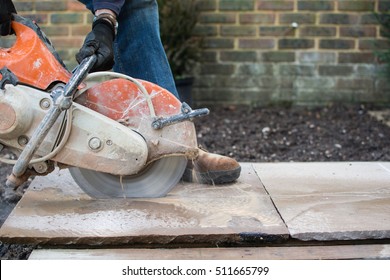 Man using the disccutter in the garden to cut the indian sandstone slabs; picture in motion, selective focus on a handle