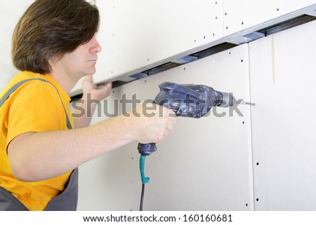 Man using drill to attach drywall panel to wall