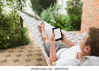 Man using a e-book or tablet computer while relaxing in a hammock. - Powered by Shutterstock