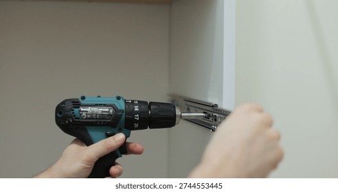 Man using a electric drill to attach a metal drawer slide to a piece of furniture during assembly. Furniture installation.