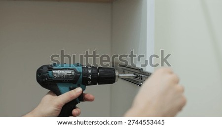 Man using a electric drill to attach a metal drawer slide to a piece of furniture during assembly. Furniture installation.