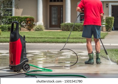 Man Using Electric Powered Pressure Washer To Power Wash Residential Concrete Driveway.