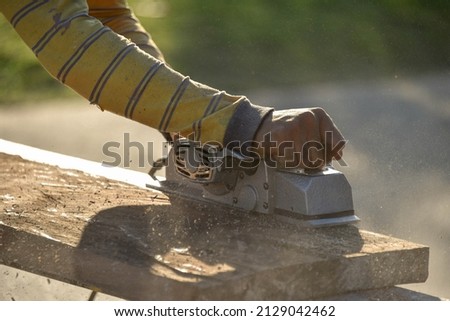 Man using electric scraper to plane wooden plank. Blur background.