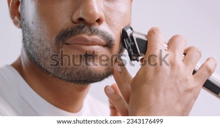 A man is using electric shaver to trim mustache and beard while standing in front of mirror in bathroom at home.