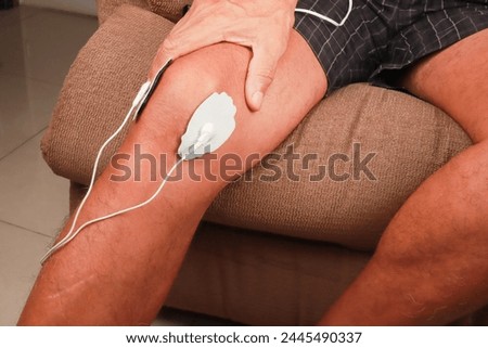 Man using an Electro Therapy Massager or Tens Unit on his knee for pain relief of Muscles and Joint