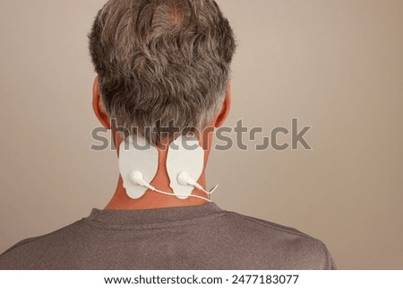 Man using a Electro Therapy Massager or Tens Unit on the back of his neck for pain relief for a migraine headache 