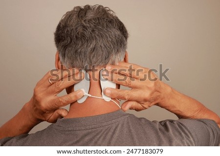Man using a Electro Therapy Massager or Tens Unit on the back of his neck for pain relief for a migraine headache 