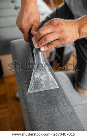 Man using an extractor vacuum cleaner tool for deep cleaning couch armrest