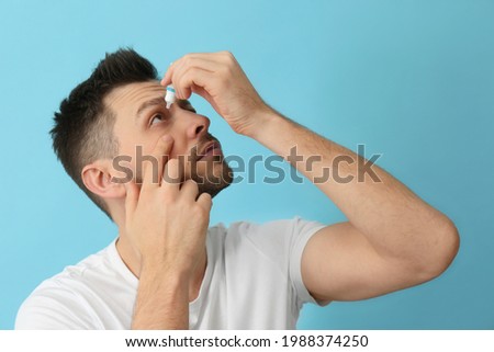 Man using eye drops on light blue background