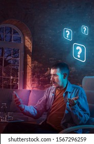 Man Using Gadget And Receive Neon Notifications At Home At Night. Sitting On Armchair, Serfing In Internet And Looking For Information. Social Media Abusing, Chatting And Browsing, Gadget Addiction.