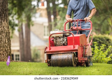 Man Using Gas Powered Aerating Machine To Aerate Residential Grass Yard. Groundskeeper Using Turf Aeration Equipment For Lawn Maintenance.