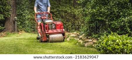 Man using gas powered aerating machine to aerate residential grass yard. Groundskeeper using turf aeration equipment for lawn maintenance.