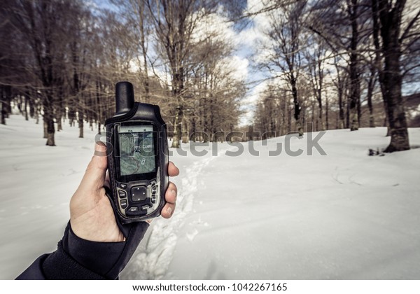 Man\
using a GPS device in a snowy forest. Hiker checking GPS\
information. Footprints in the snow. Winter\
landscape